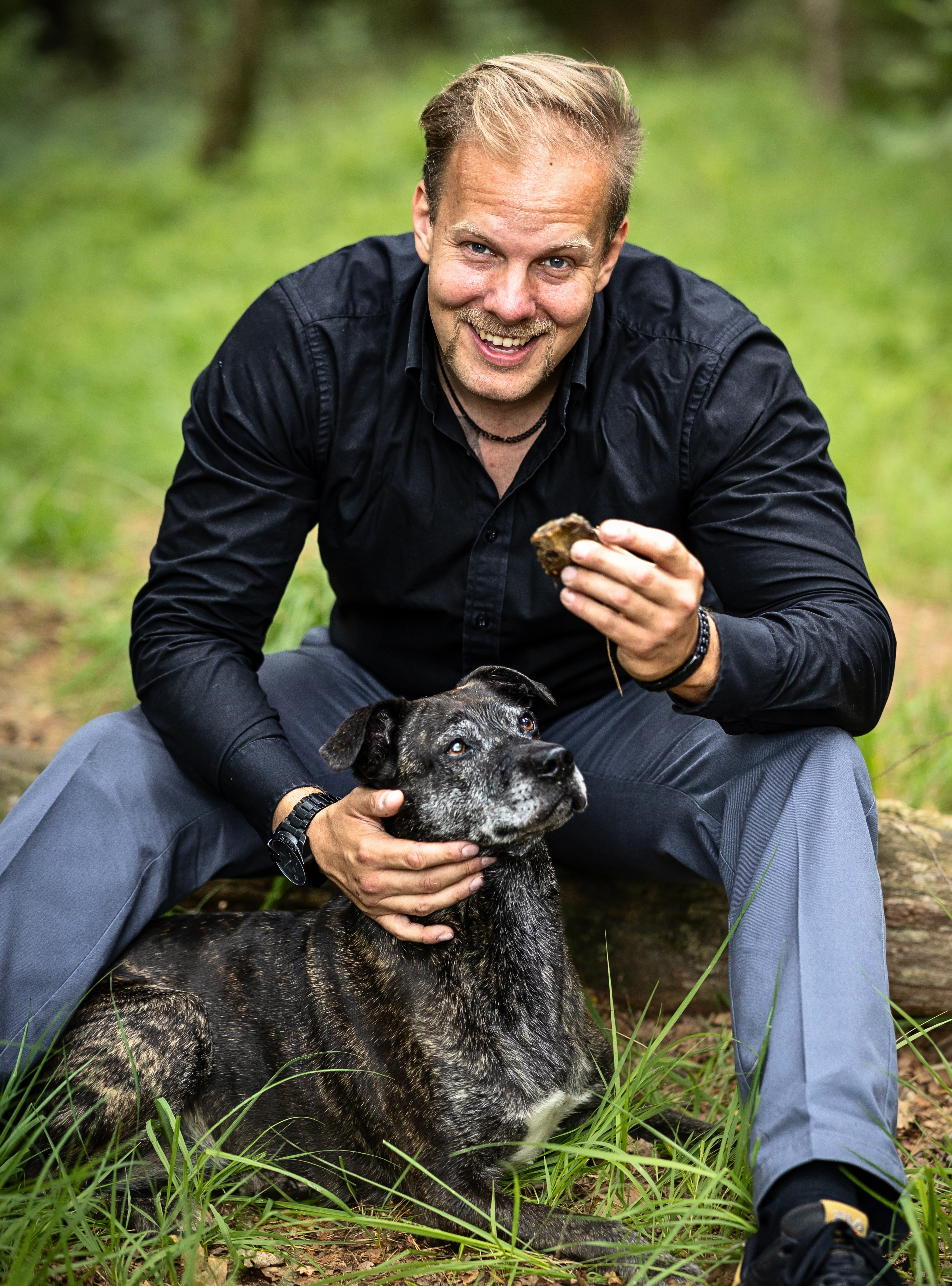 Tom Bolluck sitzt mit seinem Hund im Grünen